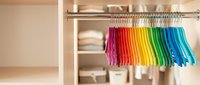 Colorful rainbow clothes hanging on rack in organized wardrobe closet. Bright garments arranged by color spectrum for home organization and storage solutions.