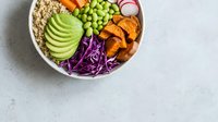 Colorful vegan Buddha bowl with quinoa, avocado, edamame, sweet potato, red cabbage, and radish on a light gray background, top view.