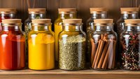 Glass jars filled with colorful spices and herbs arranged on wooden shelf for cooking and culinary seasoning in kitchen pantry storage organization.