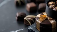 Dark chocolate pralines and truffles with gold ribbon on black background. Luxury handmade confectionery with various fillings and decorative elements. Sweet gourmet dessert.