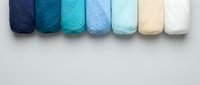 Colorful yarn skeins arranged in gradient from navy blue to white on neutral background for crafting and knitting projects.