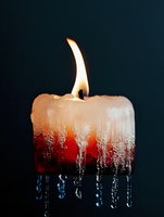 Burning white candle with melting wax dripping dramatically in icicle formations against dark background, creating atmospheric mood lighting effect.