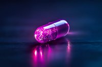 Glowing pink medical capsule with sparkles and reflections on dark surface, futuristic pharmaceutical concept with neon lighting effects and dramatic atmosphere.
