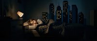 Young woman sleeping peacefully in bed with warm lamp light against dramatic city skyline backdrop at night creating cozy bedroom atmosphere.