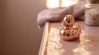 Copper rubber duck toy floating in warm bathwater with soft golden lighting creating relaxing spa atmosphere for wellness and self-care moments.