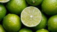 Fresh green limes background with one cut lime showing juicy flesh texture, close up view. Natural citrus fruit pattern for healthy eating and cocktail design.