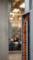 Orange fiber optic cables organized in server rack panel with blurred data center background for technology and networking infrastructure projects.