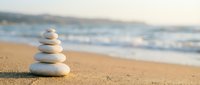 Zen stone stack balanced on sandy beach with ocean waves in soft focus background creating peaceful meditation and mindfulness atmosphere for wellness concepts.