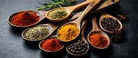 Colorful assortment of aromatic spices in wooden spoons on dark stone surface, including turmeric, paprika, pepper, and herbs for cooking.