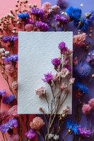 Blank textured card with dried purple and pink flowers on colorful floral background, perfect for wedding invitations or greeting cards.