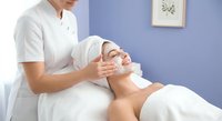 Professional spa therapist performing relaxing facial massage treatment on female client in modern wellness center with calming purple interior design.