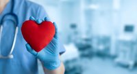Healthcare professional in blue scrubs and gloves holding red heart symbol in modern medical facility for cardiology and patient care concepts.