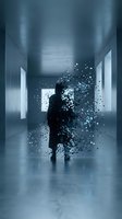 Man in dark suit standing in modern corridor dissolving into particles of light, representing digital transformation, data dispersion, and virtual existence in contemporary business environments.