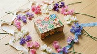 Decorative wooden jewelry box with floral painting surrounded by colorful sweet pea flowers and satin ribbons on natural wood surface for crafting.
