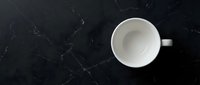 Empty white ceramic mug on dark marble surface with veining pattern, overhead view, isolated for mockup and branding design use.