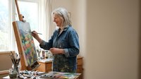 Senior Caucasian woman artist painting colorful landscape on canvas in bright home studio, creative hobby and artistic expression for mature adults.