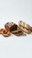 Assorted fresh baked goods including artisan bread loaves, sliced rye bread, soft pretzels and rosemary garnish isolated on white background for bakery and food design projects.