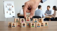 Business executive selecting diverse team members from wooden blocks with employee portraits for corporate training and development programs.