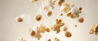 Popcorn kernels and fluffy white popped corn exploding in mid-air against neutral background, perfect for snack food advertising and cinema concepts.