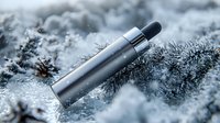 Metallic silver vape device on frosty winter pine branches with snow and ice crystals in cold blue tones, macro photography for vaping and smoking cessation concept.