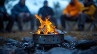 Bright orange flames dance in portable fire pit during evening camping, with blurred people gathered around creating cozy outdoor atmosphere.