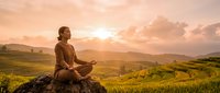 Young Asian man practicing meditation in lotus position on mountain rock during golden sunset over terraced rice fields landscape for mindfulness wellness.