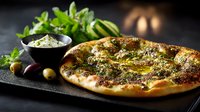 Fresh baked za'atar flatbread with olive oil and herbs served on dark stone board with fresh mint leaves and traditional dipping sauce.