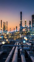 Industrial oil refinery complex at twilight with illuminated processing towers and pipeline infrastructure against colorful sunset sky for energy concepts.