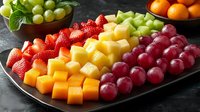 Fresh fruit platter with colorful arrangement of strawberries, pineapple chunks, cantaloupe cubes and red grapes on dark plate, garnished with mint leaves.