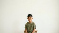 Young Asian boy wearing olive green t-shirt smiling at camera against white background, suitable for family, education, and lifestyle design projects.