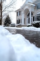 Elegant white colonial style house entrance with snow covered driveway and landscaping, featuring classical columns and arched doorway in winter setting.