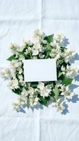 White jasmine flowers arranged in circular wreath with blank card on white marble background, ideal for wedding invitations, greeting cards, and spring event designs.