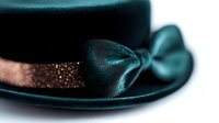 Elegant dark teal top hat with decorative bow and glittering copper ribbon band against white background, perfect for fashion accessories and formal attire.