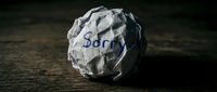 Crumpled paper ball with the word Sorry written on it, placed on a dark wooden surface, symbolizing regret and apology.