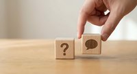 Hand placing wooden blocks with question mark and speech bubble symbols on desk representing communication and problem solving concepts.