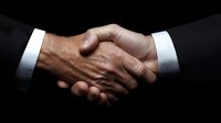 Professional business handshake between two men wearing dark suits and white shirts against black background, symbolizing partnership, agreement and trust in corporate setting.