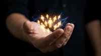 Young adult male with light skin tone holding glowing golden light bulbs in cupped hands against dark background, symbolizing innovation, ideas, and creative energy for business concepts.