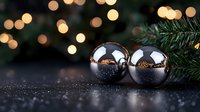 Shiny silver Christmas baubles on dark surface with golden bokeh lights and pine branches, festive holiday decoration with reflection and copy space.