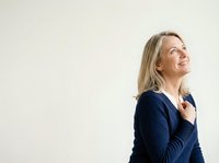 Mature woman with long blonde hair wearing dark navy cardigan, looking upward with confident smile against neutral background. Professional portrait for business, corporate, and lifestyle use.