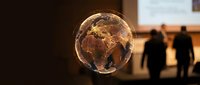 Glowing golden Earth globe with illuminated continents floating in modern office space with silhouetted business people walking in background.