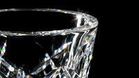 Crystal clear cut glass tumbler with prismatic light reflections on black background for luxury beverage photography and elegant drinkware designs.