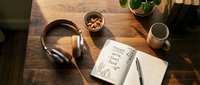 Cozy wooden desk flat lay with headphones, open notebook with today to-do list, snacks, mug, and plant in warm morning light.