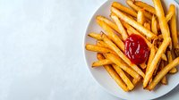 Golden crispy french fries served on white ceramic plate with red ketchup sauce, shot from above on light background. Perfect for restaurant menu or food delivery.