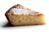 Slice of homemade vanilla sponge cake dusted with powdered sugar on white background, isolated macro shot showing soft moist texture and golden crust.
