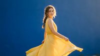Young woman in flowing yellow dress dancing with dramatic movement against blue gradient background for fashion and lifestyle projects.
