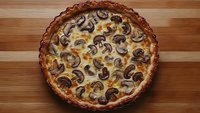 Homemade mushroom quiche with golden crust on wooden cutting board, savory egg custard filling with sliced mushrooms for brunch or dinner.