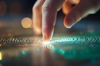 Finger touching rippling water surface creating concentric circles with magical light effect and turquoise reflections against dark background with bokeh lights.