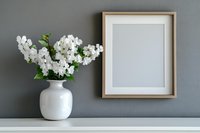 White orchids in ceramic vase next to empty wooden frame on shelf against gray wall. Minimalist home decor composition for modern interior design.