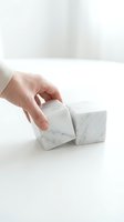 Hand reaching for white marble geometric blocks on clean surface for modern interior design and minimalist home decor styling concepts.