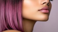 Close up profile of African American woman with pink hair and glossy lips against soft purple background, showcasing modern beauty and hair coloring trends.